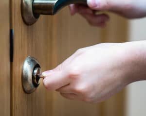 Main insérant une clé dans une serrure de porte en bois, l'autre main sur la poignée. Action d'ouvrir ou de fermer.