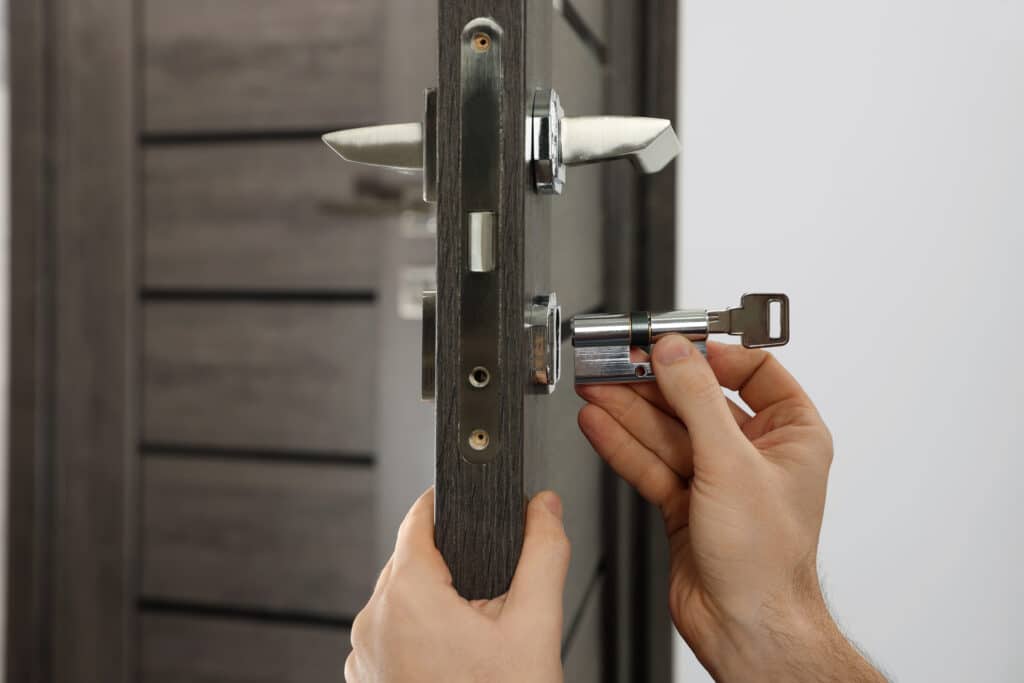 Des mains installent un cylindre de serrure métallique avec une clé dans une porte en bois sombre. Remplacement de serrure.