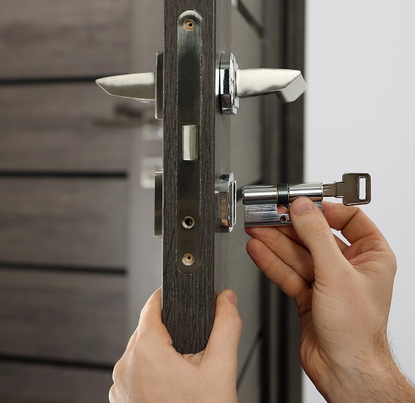 Mains installant un cylindre de serrure avec clé dans une porte en bois gris foncé. Dépannage ou remplacement de serrure.